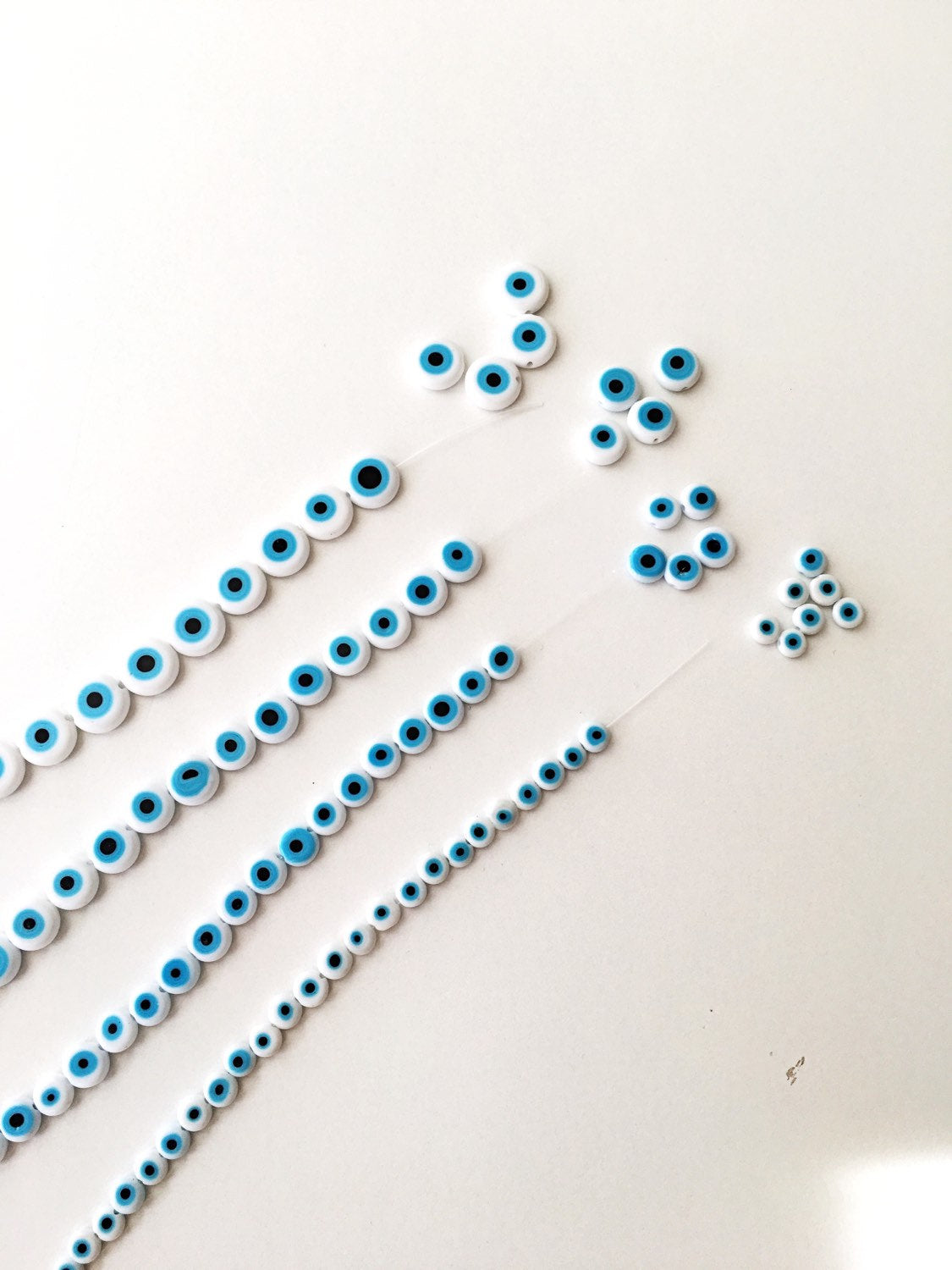 A collection of white evil eye beads in various sizes from 6mm to 12mm, showcasing their unique handmade designs.