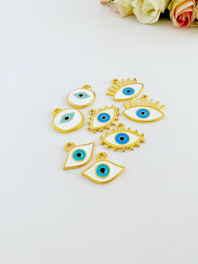 A collection of White Evil Eye Charms in various styles, showcasing their brass material and intricate designs.