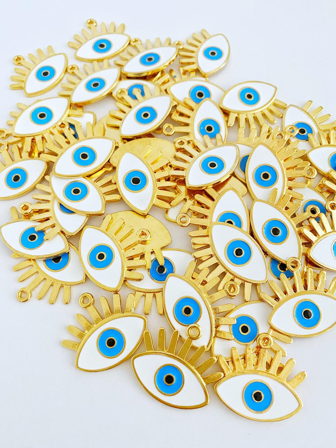 A collection of White Evil Eye Charms in various styles, showcasing their brass material and intricate designs.