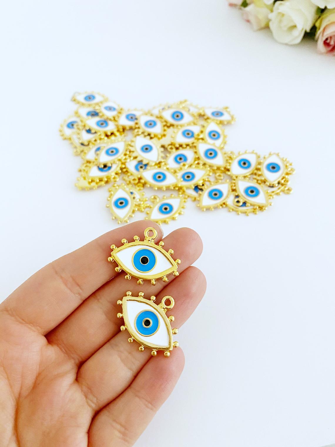 A collection of White Evil Eye Charms in various styles, showcasing their brass material and intricate designs.