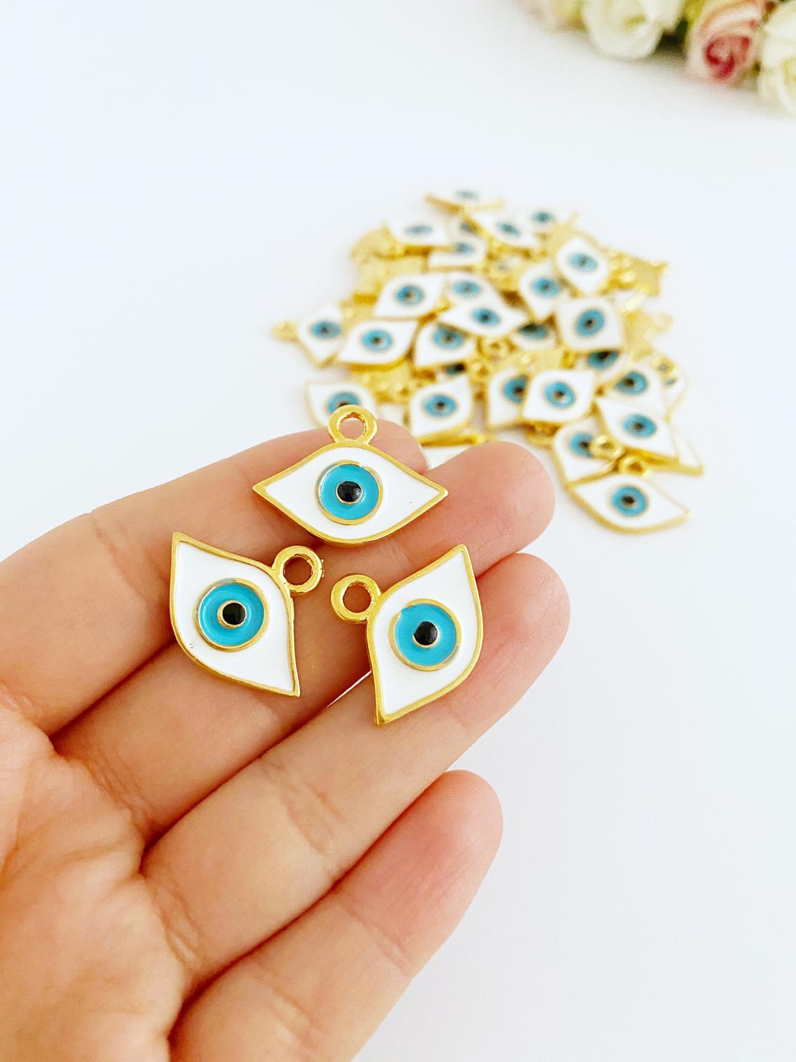 A collection of White Evil Eye Charms in various styles, showcasing their brass material and intricate designs.