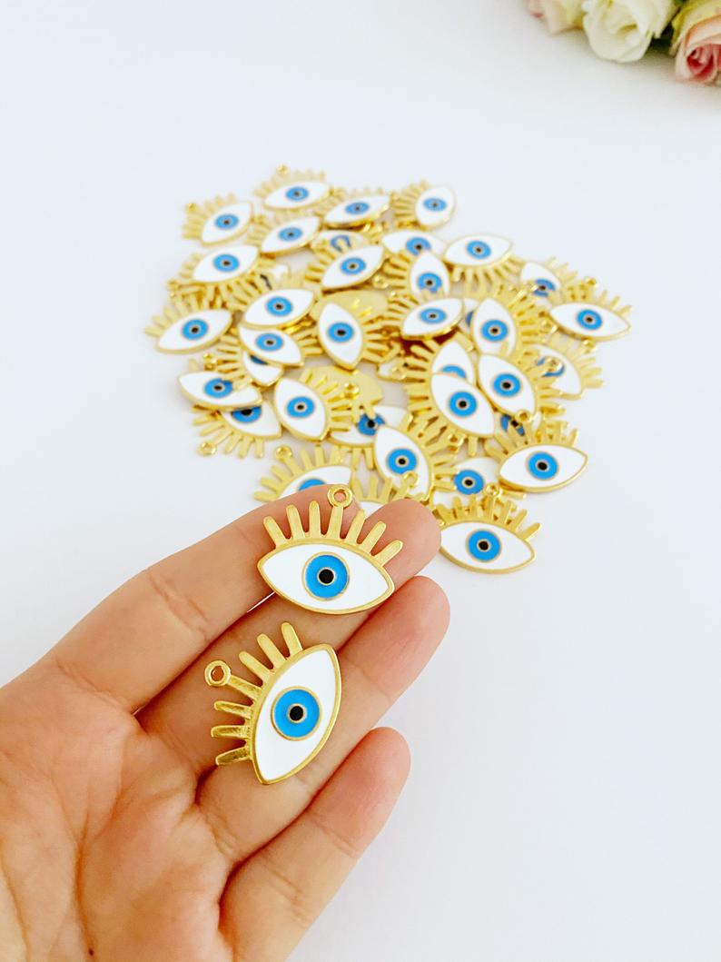 A collection of White Evil Eye Charms in various styles, showcasing their brass material and intricate designs.