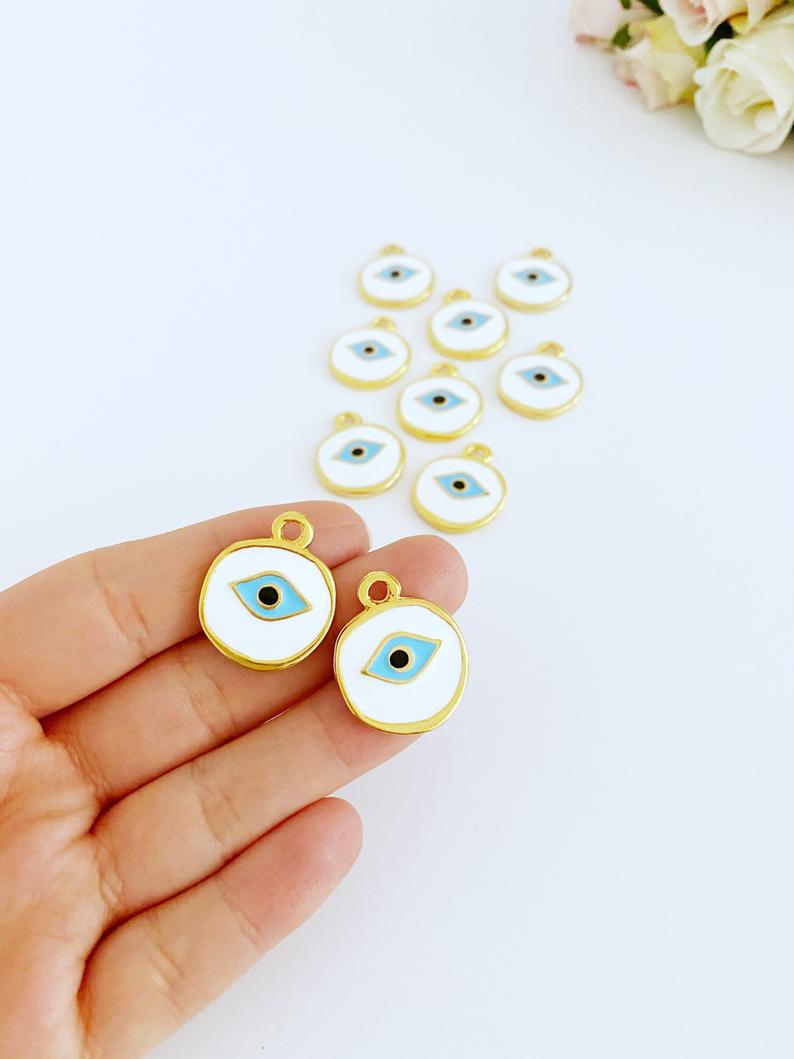 A collection of White Evil Eye Charms in various styles, showcasing their brass material and intricate designs.