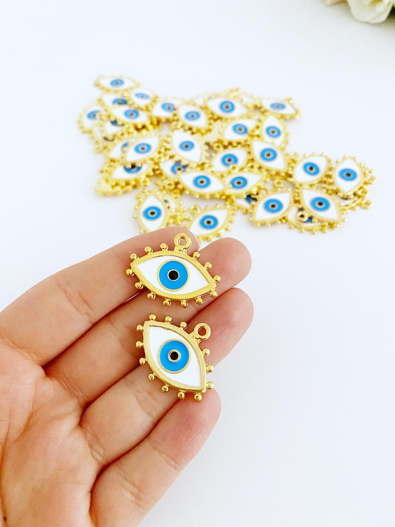 A beautiful White Evil Eye Charm featuring an enamel bead design with a gold evil eye pendant, perfect for jewelry making.