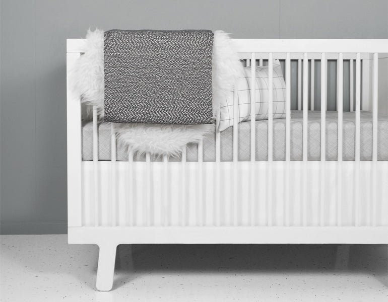Avi Deluxe Crib Bedding Set featuring a grey organic cotton blanket, Nest Sheet, White Crib Skirt, and Nest baby blanket, designed for modern nurseries.