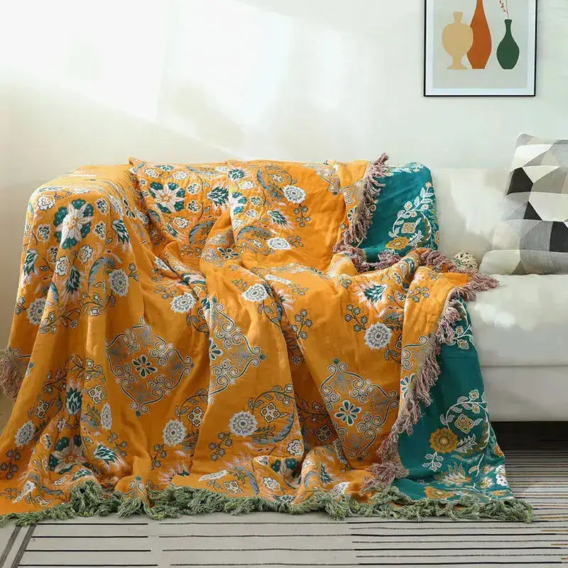 A vibrant yellow-orange Cotton Gauze Fringed Throw Blanket draped elegantly over a sofa, showcasing its soft texture and stylish fringed edges.