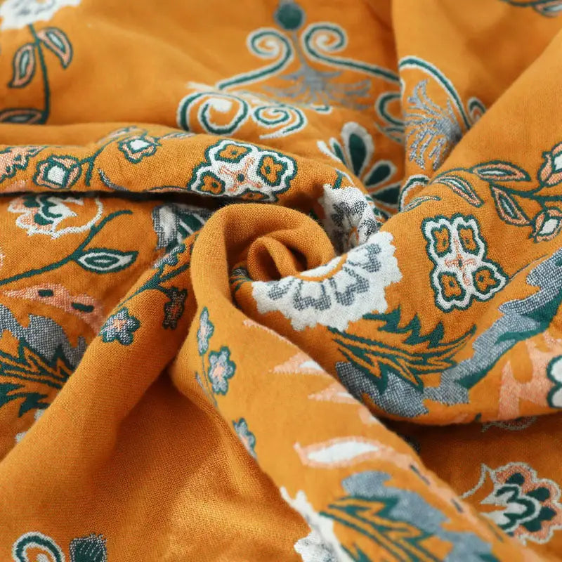 A vibrant yellow-orange Cotton Gauze Fringed Throw Blanket draped elegantly over a sofa, showcasing its soft texture and stylish fringed edges.