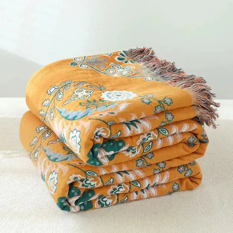 A vibrant yellow-orange Cotton Gauze Fringed Throw Blanket draped elegantly over a sofa, showcasing its soft texture and stylish fringed edges.