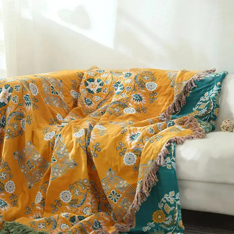 A vibrant yellow-orange Cotton Gauze Fringed Throw Blanket draped elegantly over a sofa, showcasing its soft texture and stylish fringed edges.