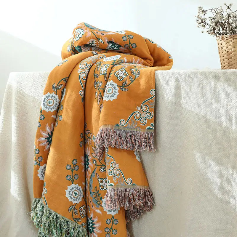 A vibrant yellow-orange Cotton Gauze Fringed Throw Blanket draped elegantly over a sofa, showcasing its soft texture and stylish fringed edges.