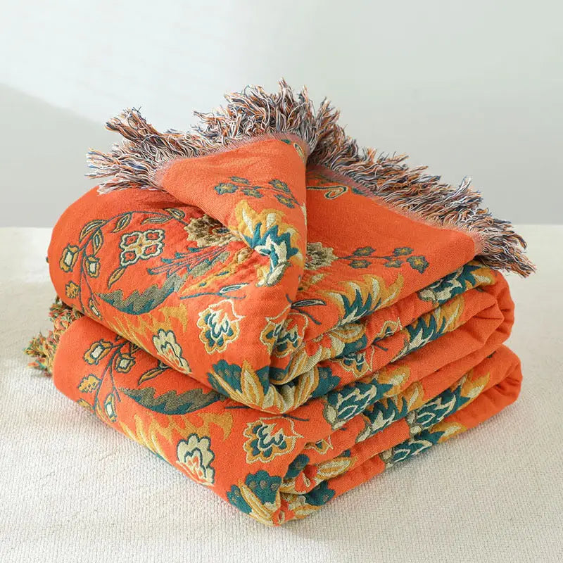A vibrant yellow-orange Cotton Gauze Fringed Throw Blanket draped elegantly over a sofa, showcasing its soft texture and stylish fringed edges.