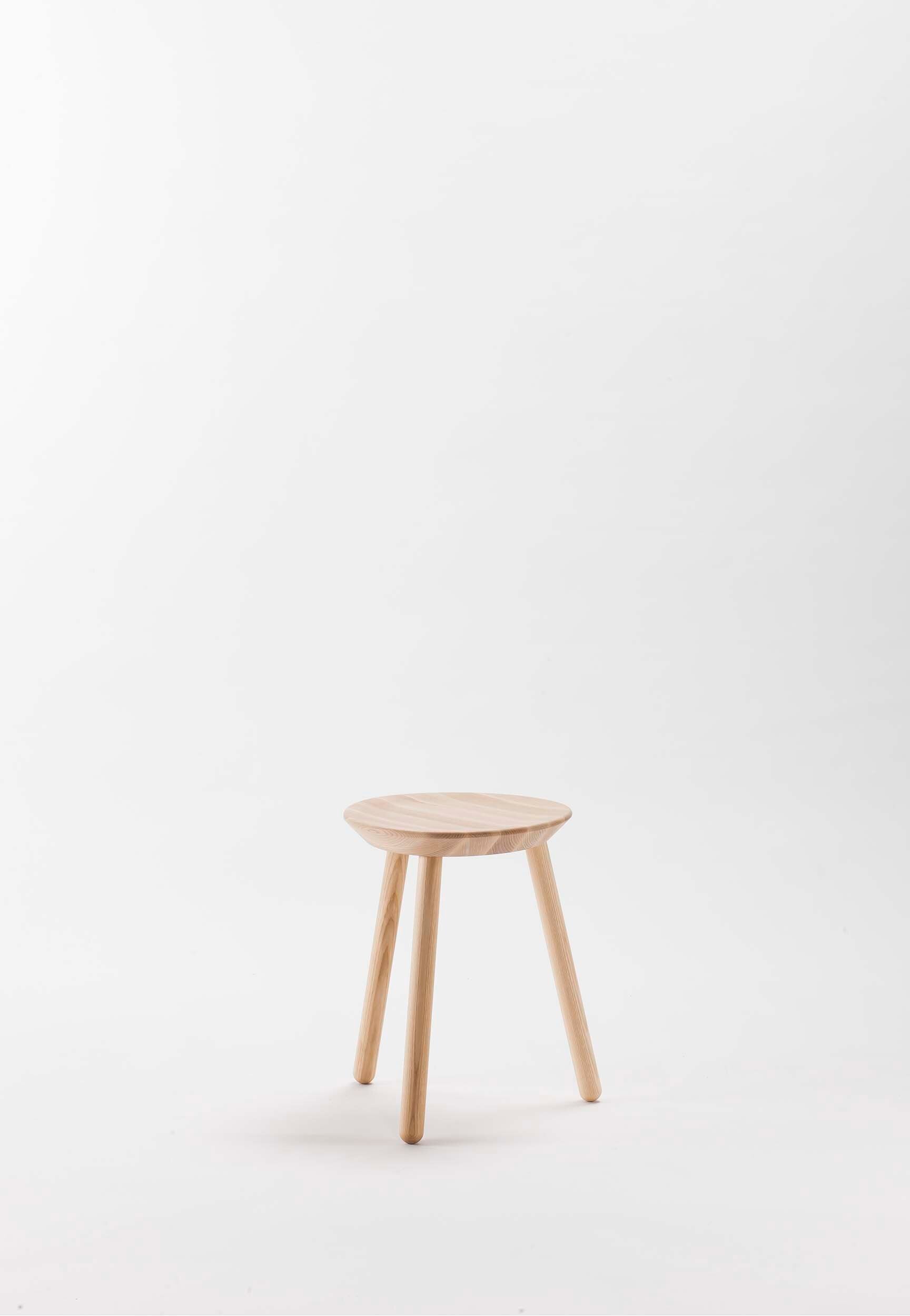 A compact Naïve Stool made of solid ash wood with three sturdy legs, showcasing its minimalist design and natural finish.