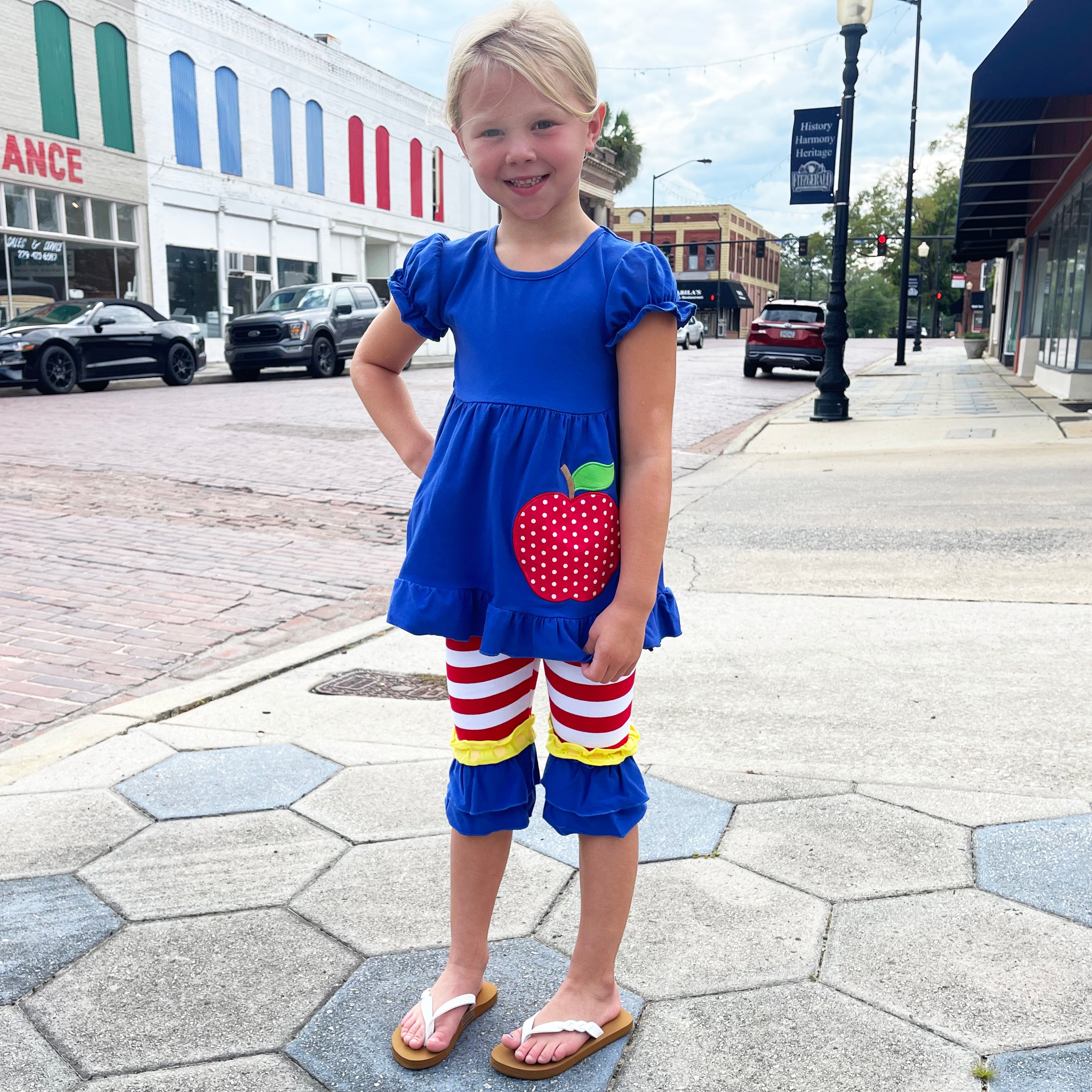 Girls Back to School Red Apple Tunic with Ruffle Pants, featuring a blue top with apple applique and red striped capri pants.