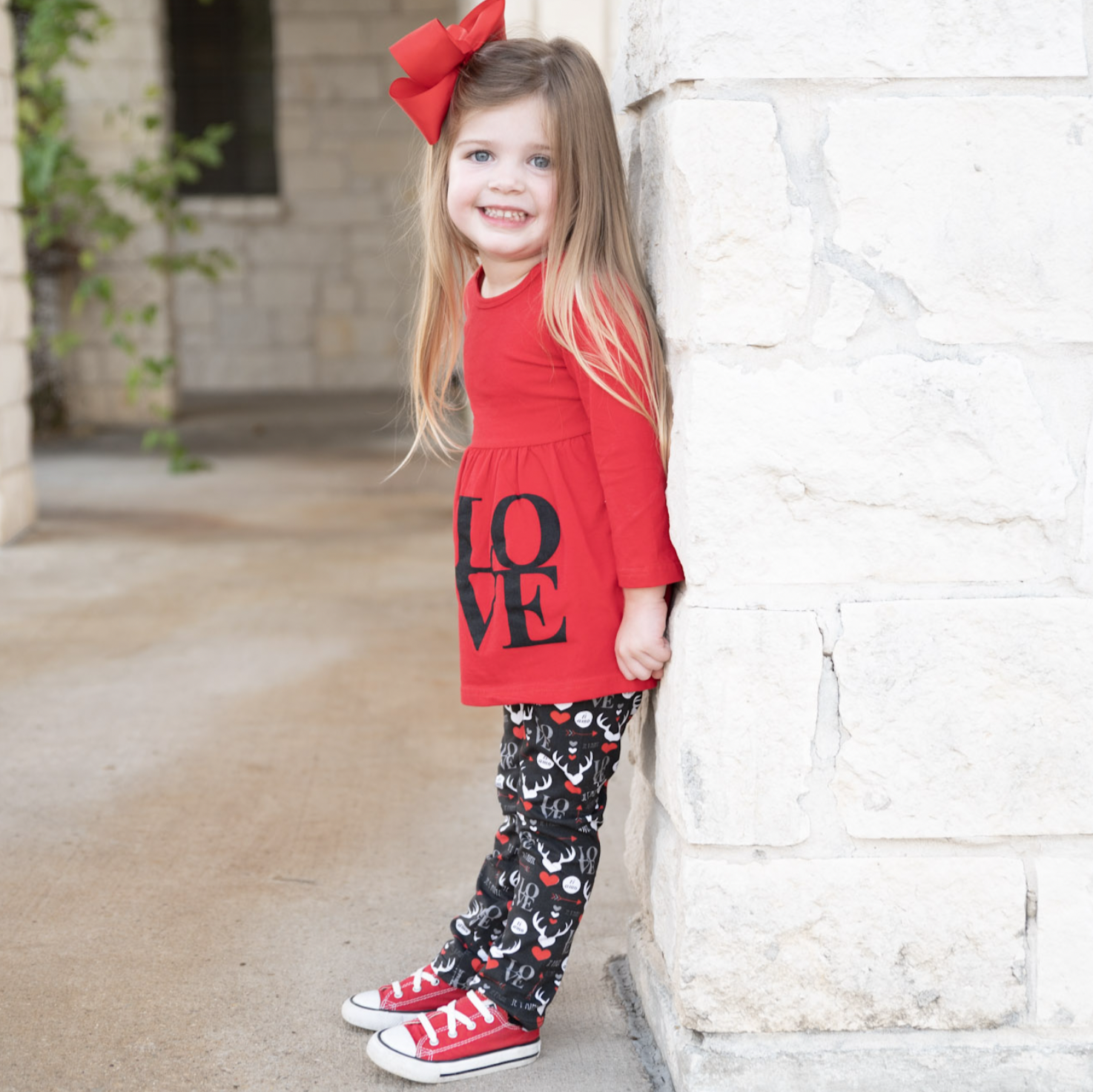 Girls Valentine's Day outfit featuring a red long sleeve tunic with LOVE applique, whimsical black leggings, and a coordinating scarf.