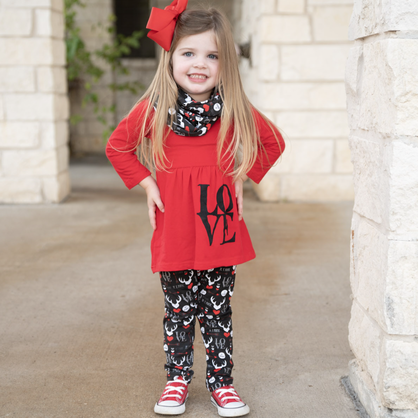 Girls Valentine's Day outfit featuring a red long sleeve tunic with LOVE applique, whimsical black leggings, and a coordinating scarf.