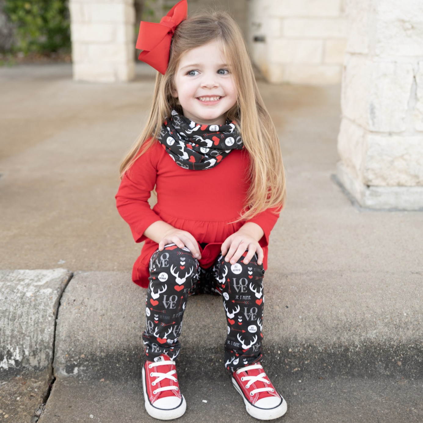 Girls Valentine's Day outfit featuring a red long sleeve tunic with LOVE applique, whimsical black leggings, and a coordinating scarf.