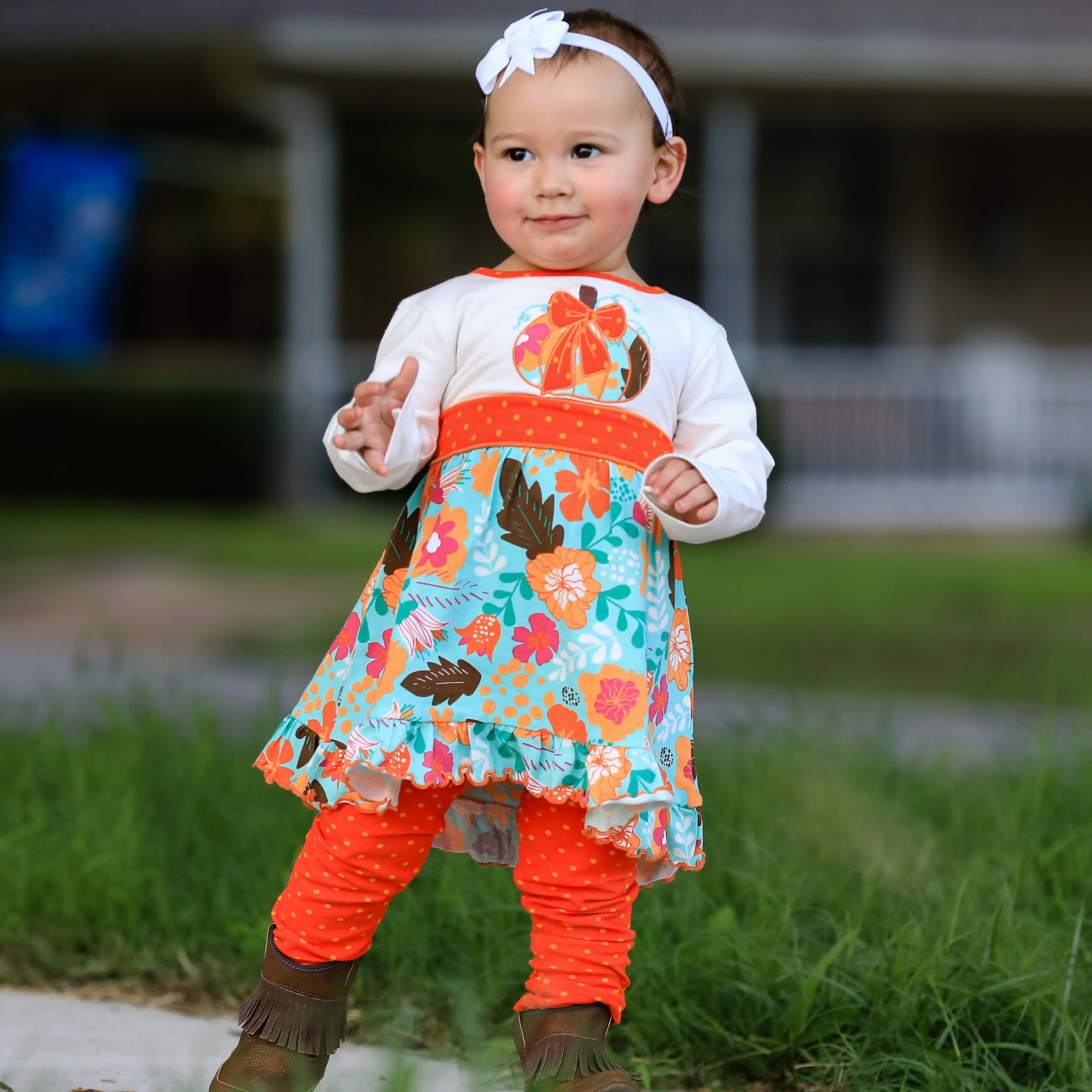 Girls vibrant autumn floral pumpkin dress with leggings, featuring a cream tunic with an embroidered pumpkin patch and orange polka dot ruffle.