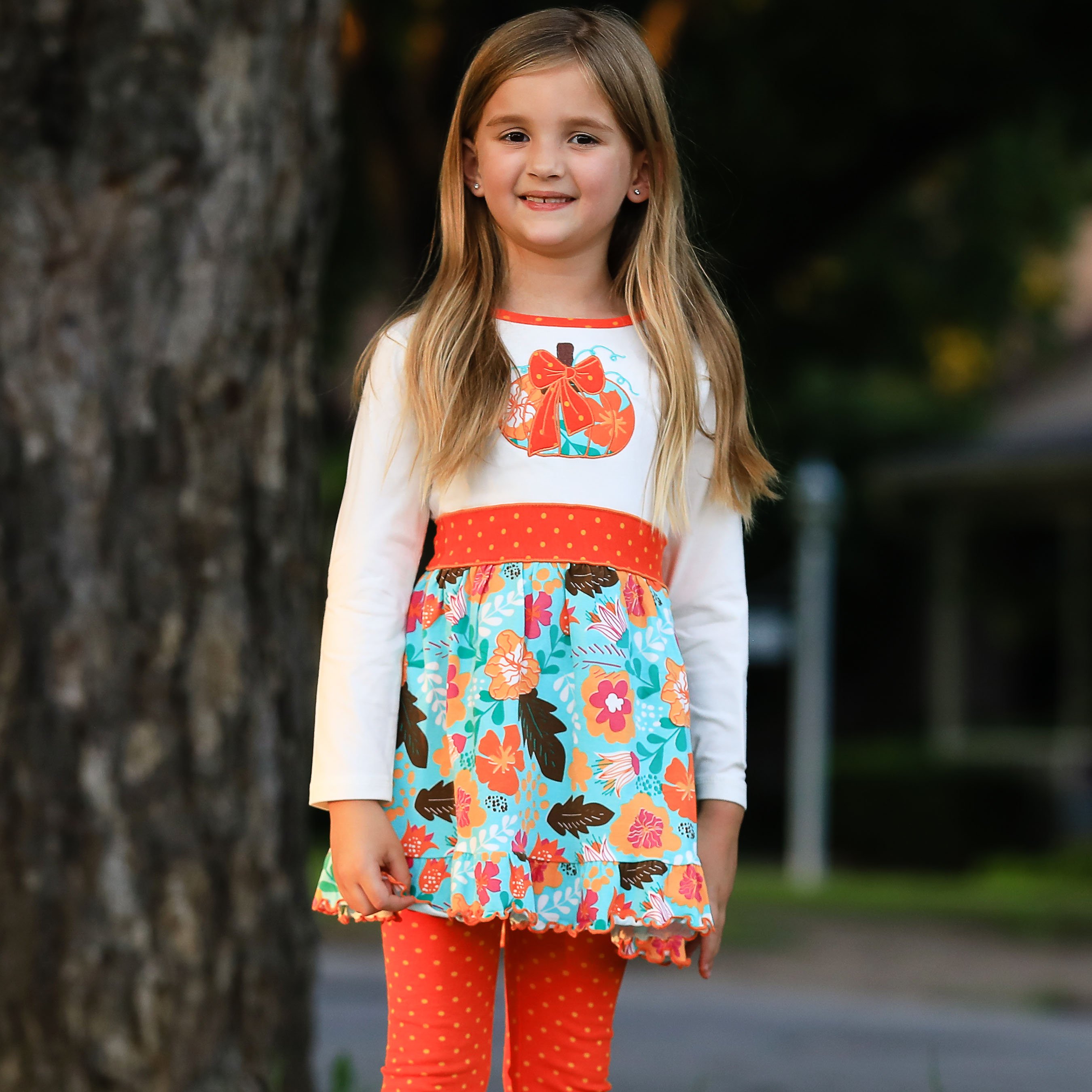 Girls vibrant autumn floral pumpkin dress with leggings, featuring a cream tunic with an embroidered pumpkin patch and orange polka dot ruffle.