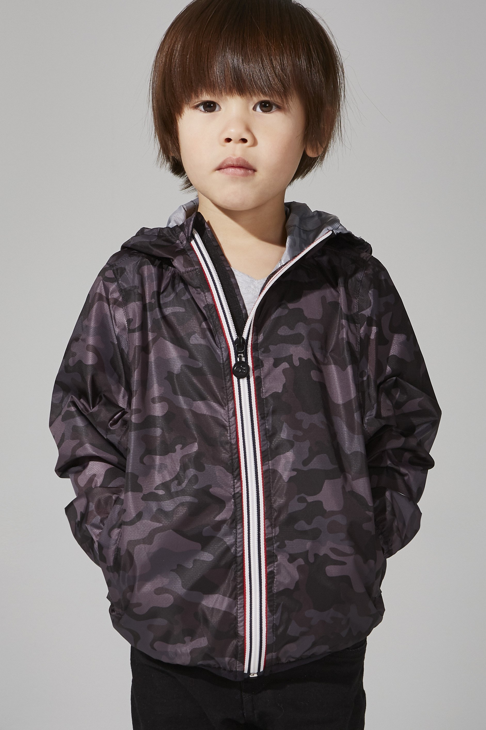 Kids black camo full zip packable rain jacket displayed on a hanger, showcasing its stylish design and functional features.