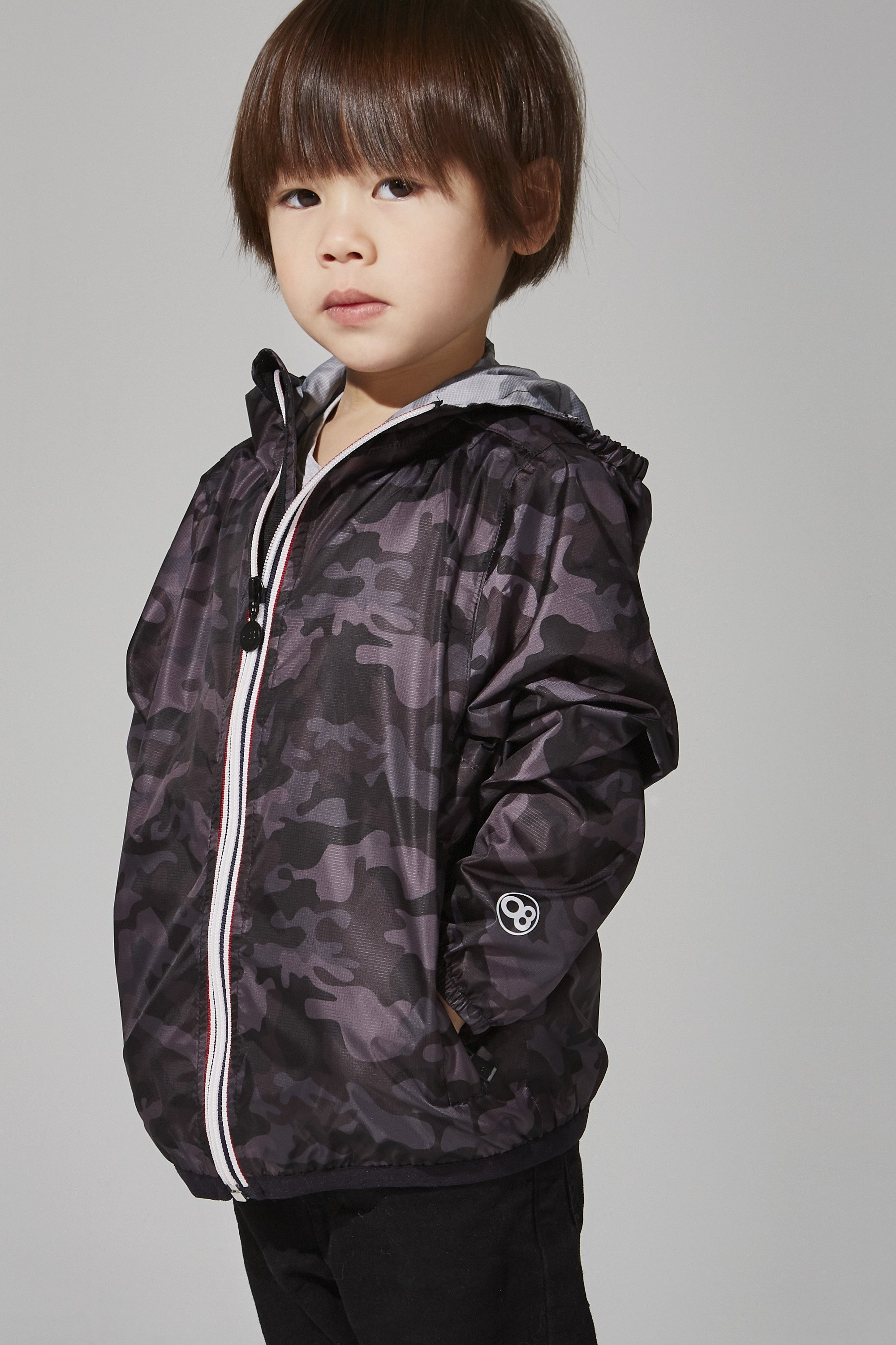 Kids black camo full zip packable rain jacket displayed on a hanger, showcasing its stylish design and functional features.