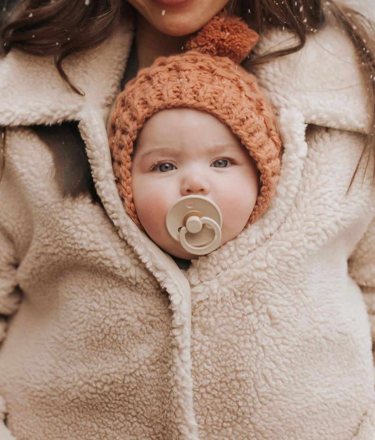 A soft ash-colored knit bonnet for infants, suitable for ages 6M to 18M, featuring a neutral gender design.