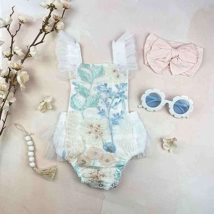 Louella embroidered romper featuring white floral design with tulle ruffles and snap closure.