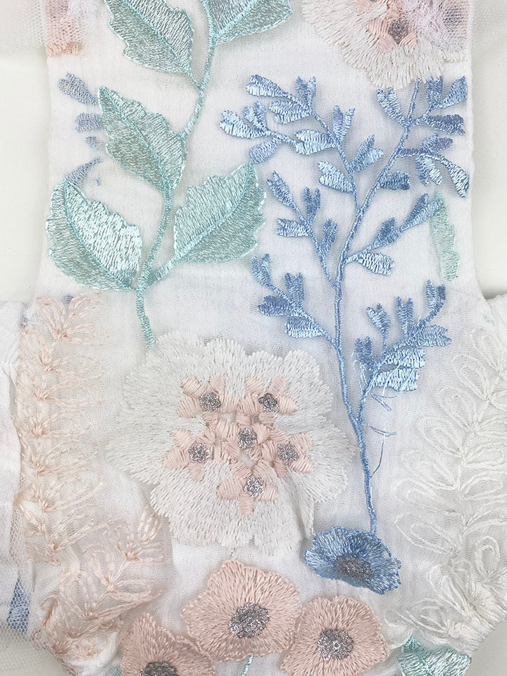 Louella embroidered romper featuring white floral design with tulle ruffles and snap closure.