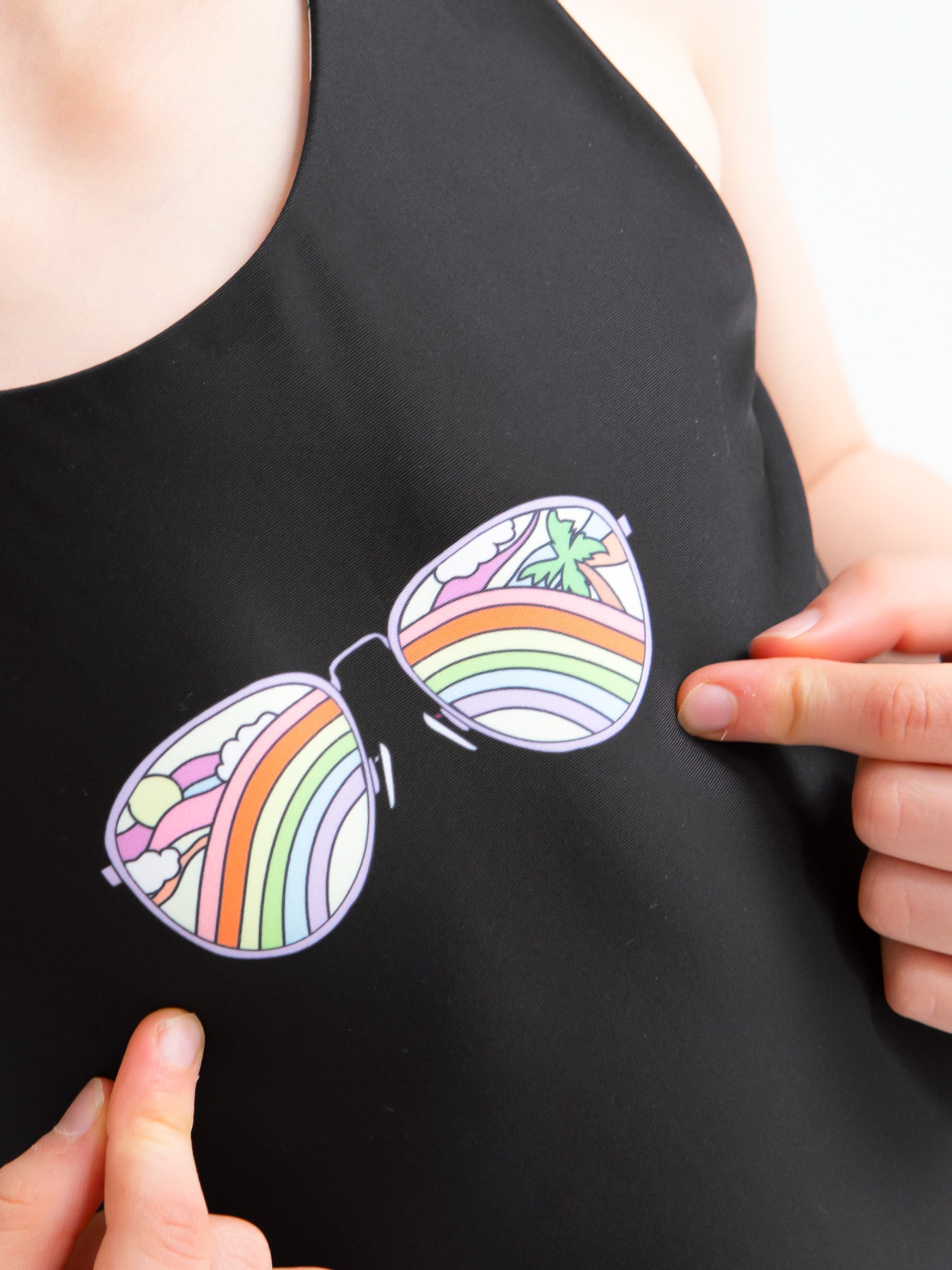 Rebel reversible one-piece swimsuit featuring a black side with sunglasses print and a colorful rainbow stripe side, designed for girls and tweens.
