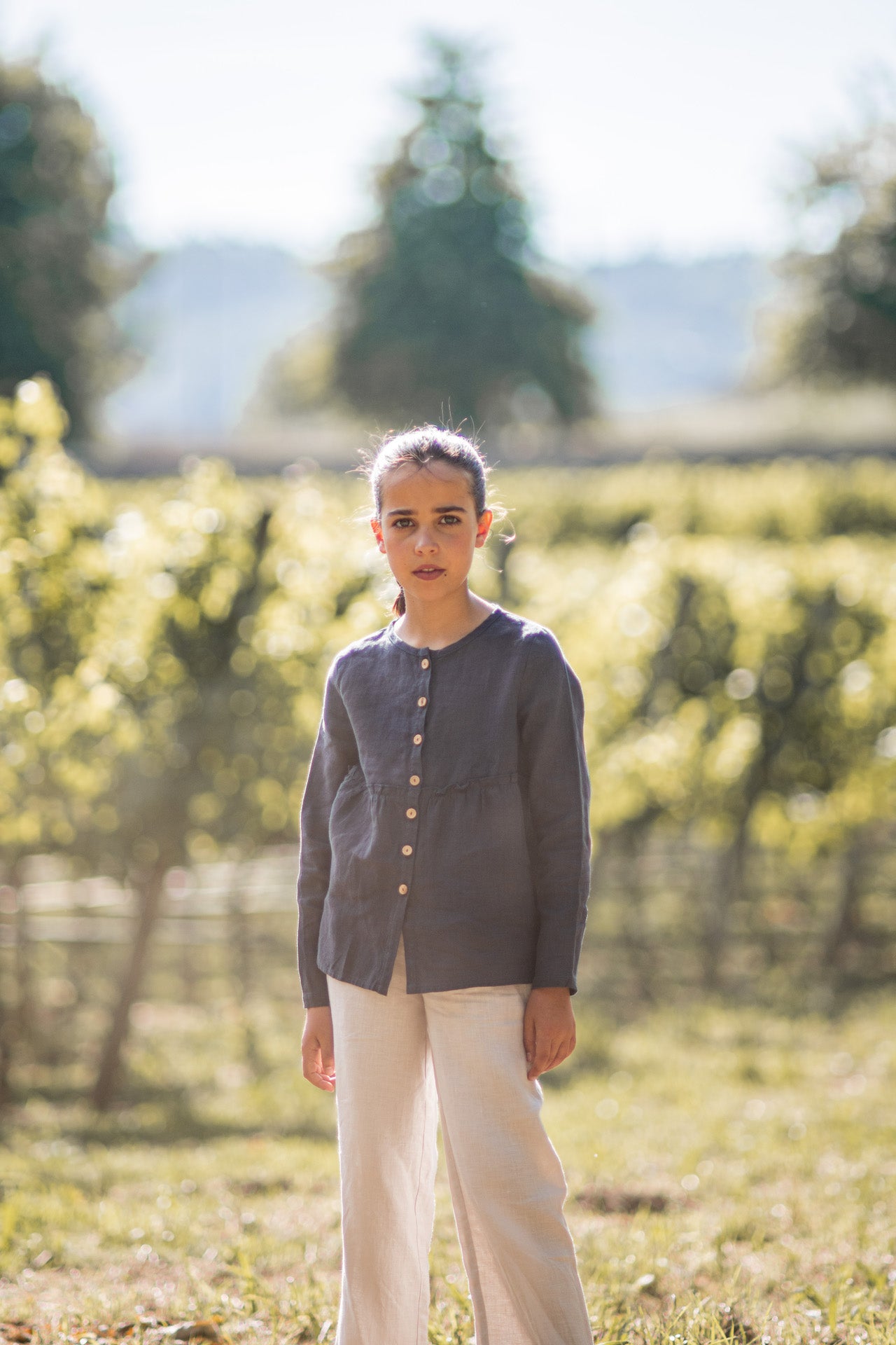 A casual long-sleeve shirt in violet blue with olive wood buttons and a frilled elasticised waist, made from lightweight linen fabric.
