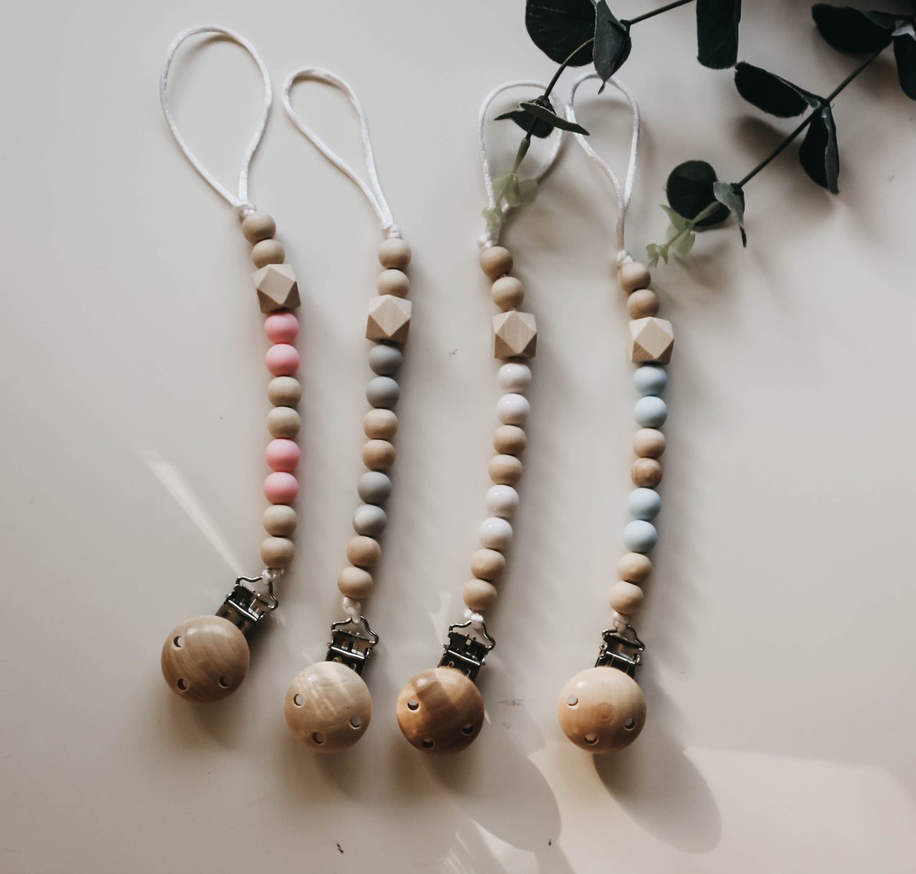 A set of colorful wooden pacifier clips, showcasing four different colors and a sturdy design for securing pacifiers.