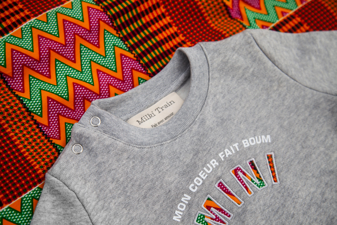 Limited Edition Mon Coeur Fait Boum Mini sweatshirt in heather grey with vibrant African Wax Fabric letters.