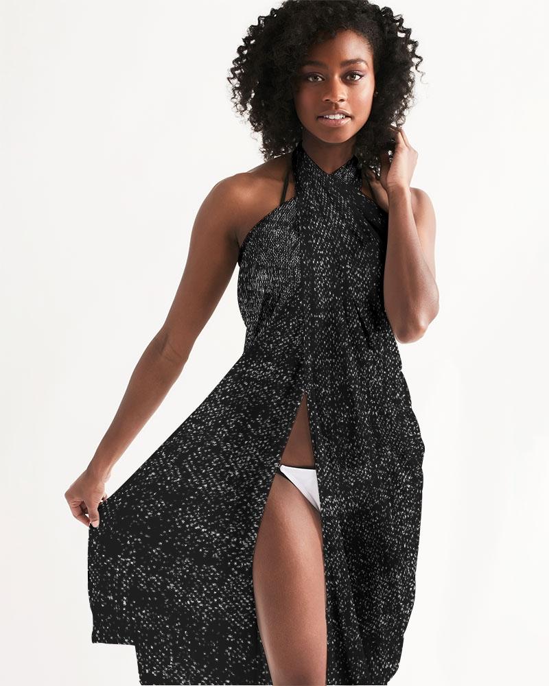 A lightweight sheer sarong swimsuit cover-up wrap in distressed black, elegantly draped over a beach chair, showcasing its flowy fabric and self-tie closure.