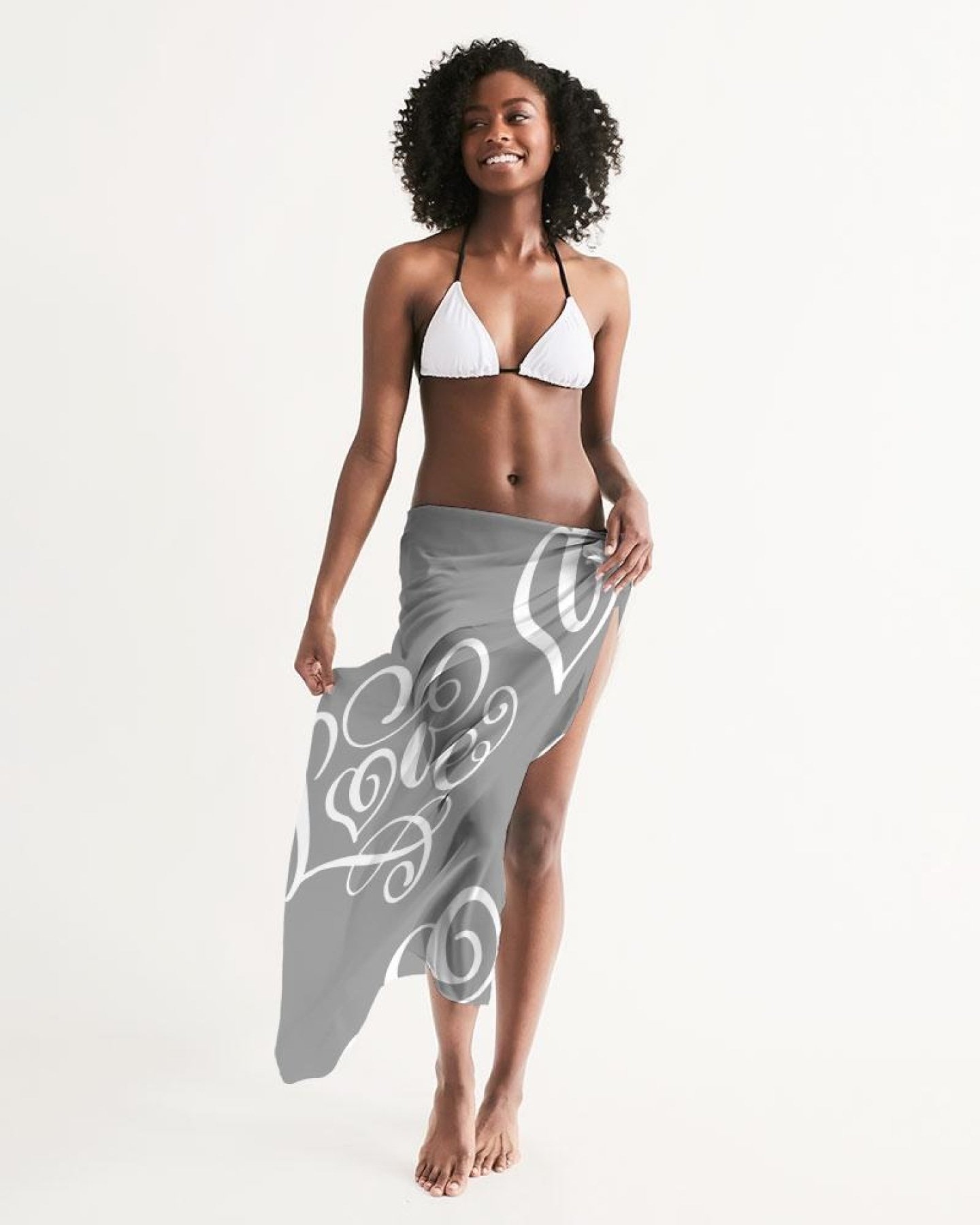 A lightweight sheer sarong swimsuit cover up wrap in Love Grey, elegantly draped over a beach chair, showcasing its flowing fabric and self-tie closure.