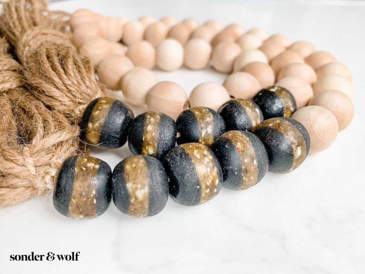 A beautifully crafted 4ft wood bead garland featuring 10 Black Kente Krobo beads and jute tassels, perfect for home decor.