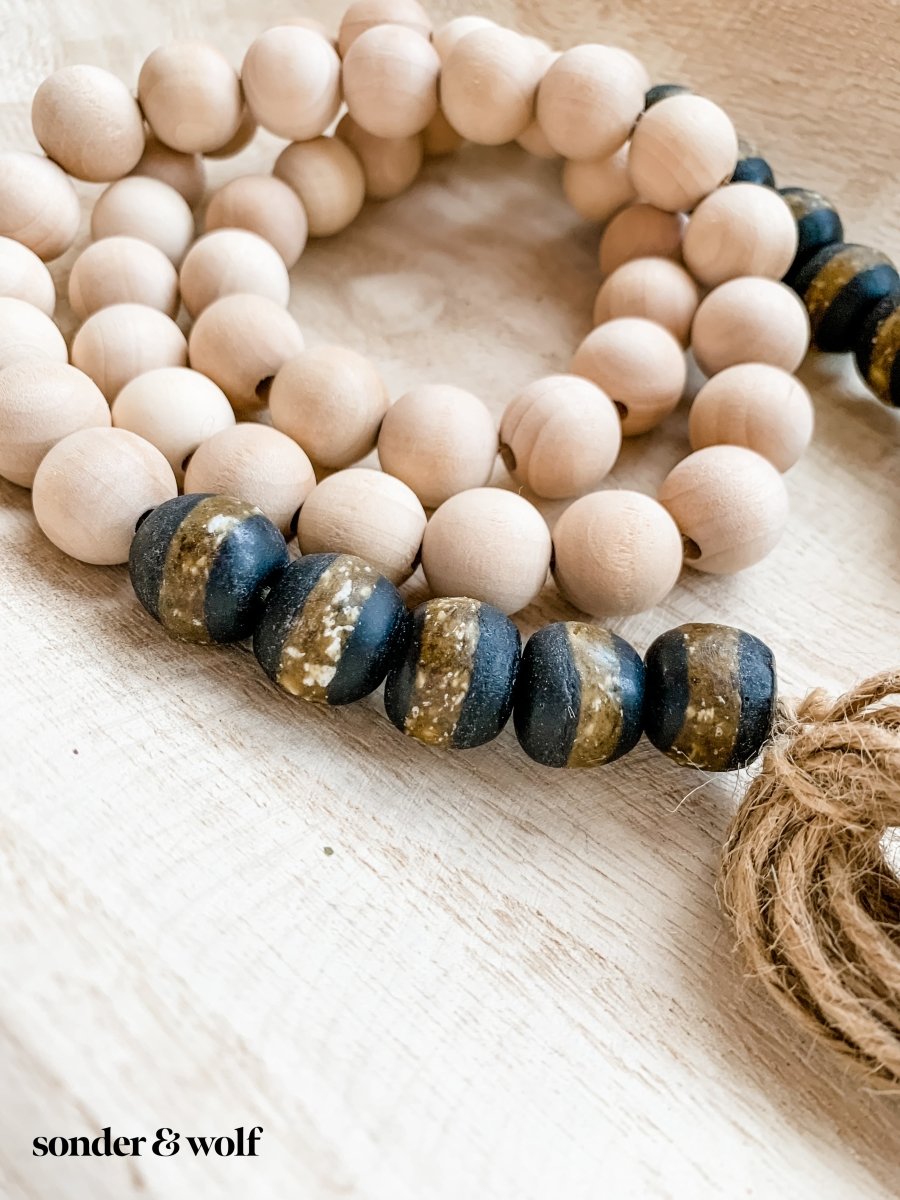 A beautifully crafted 4ft wood bead garland featuring 10 Black Kente Krobo beads and jute tassels, perfect for home decor.