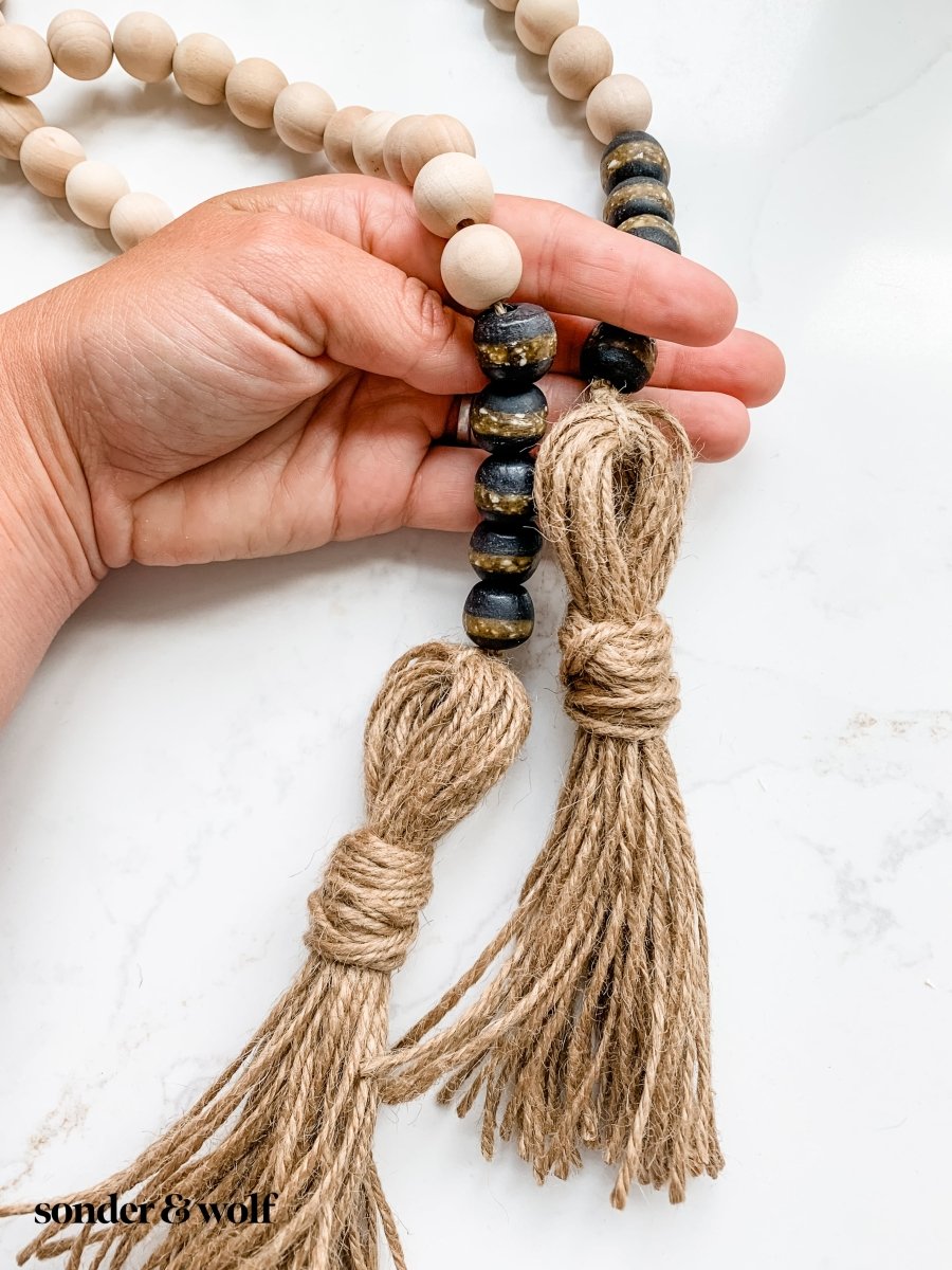 A beautifully crafted 4ft wood bead garland featuring 10 Black Kente Krobo beads and jute tassels, perfect for home decor.