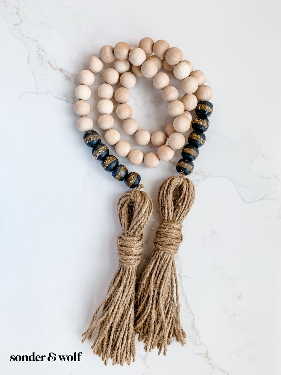 A beautifully crafted 4ft wood bead garland featuring 10 Black Kente Krobo beads and jute tassels, perfect for home decor.