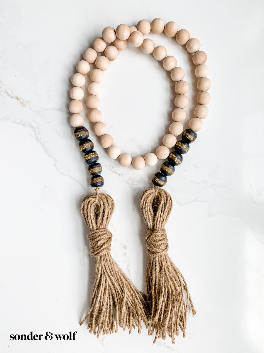 A beautifully crafted 4ft wood bead garland featuring 10 Black Kente Krobo beads and jute tassels, perfect for home decor.