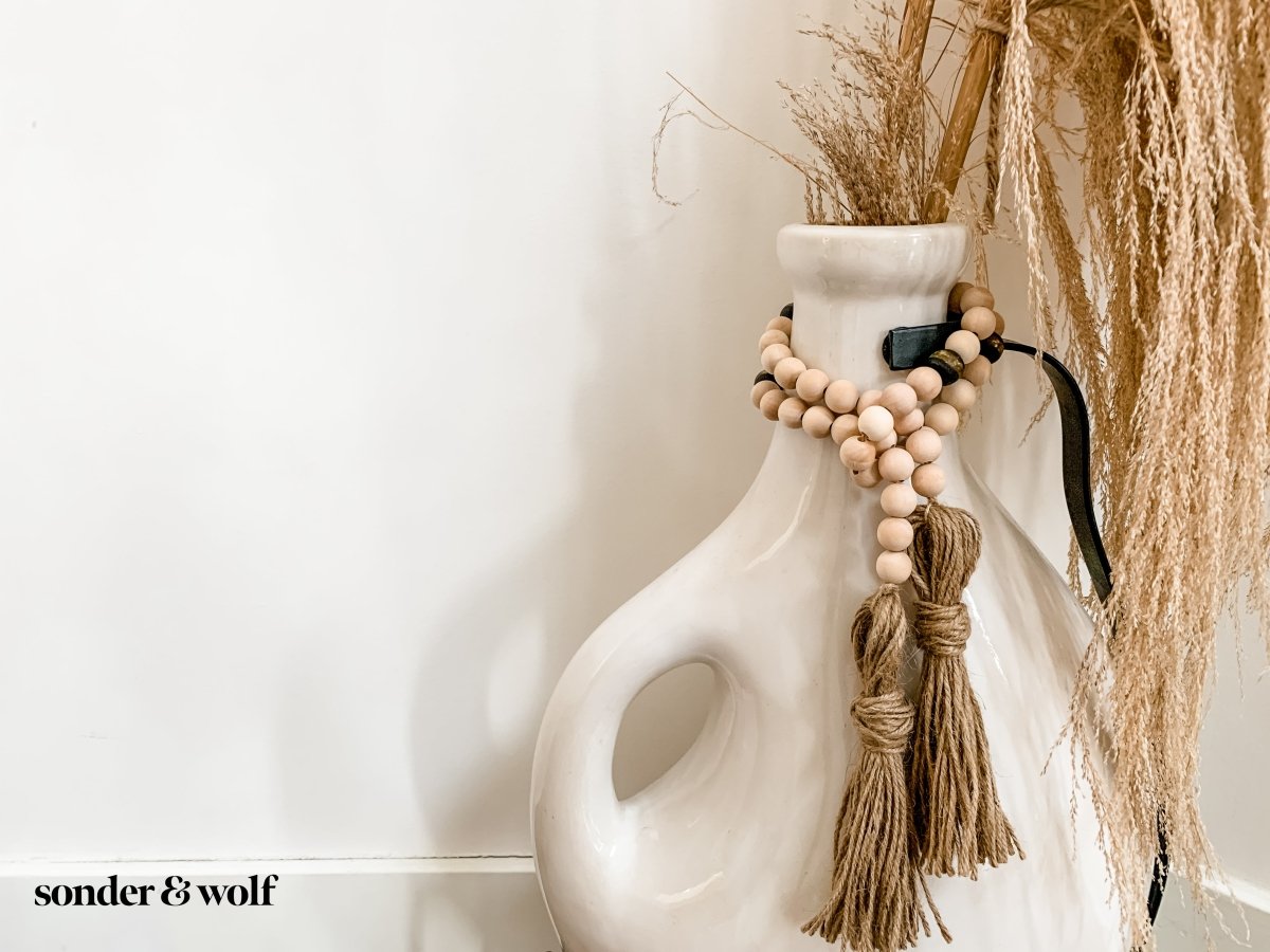 A 4ft handmade wood bead garland featuring light unfinished wood beads and four distinctive Black Kente Krobo beads, adorned with jute tassels.