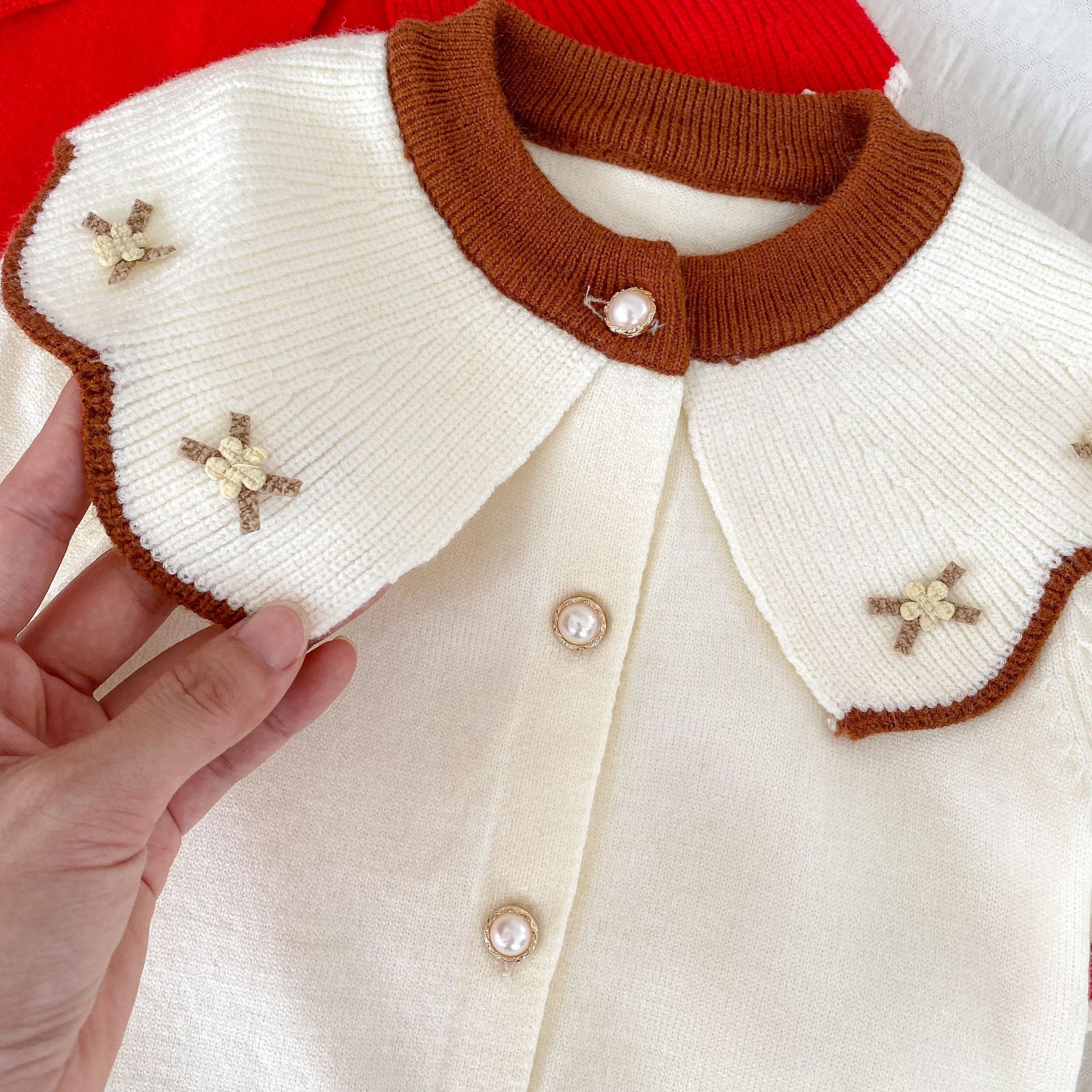 A cozy knitted top for baby girls featuring long sleeves, a floral pattern collar, available in red and apricot colors.