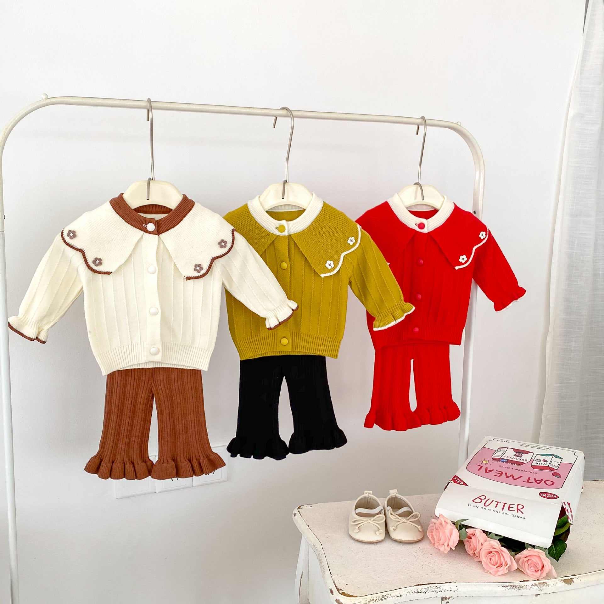 A cute baby girl wearing a long-sleeved embroidered top with flower designs in red, yellow, and beige colors, perfect for autumn.