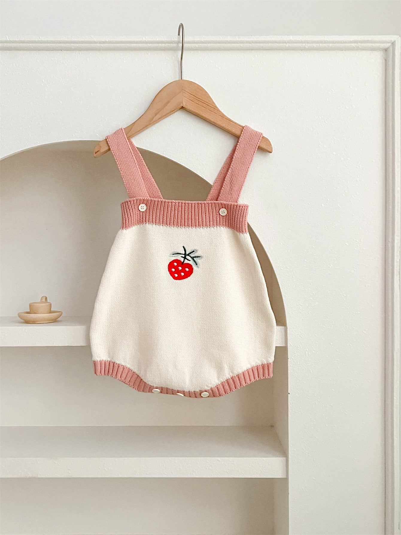 A cute baby girl wearing a long-sleeved knitted top with strawberry embroidery in red and pink colors, perfect for autumn.
