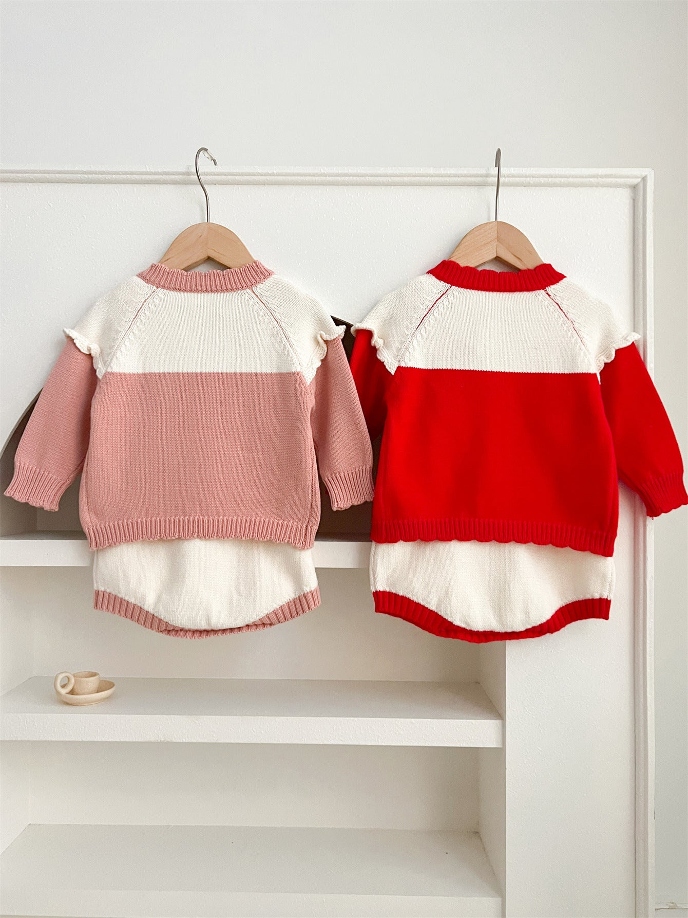 A cute baby girl wearing a long-sleeved knitted top with strawberry embroidery in red and pink colors, perfect for autumn.