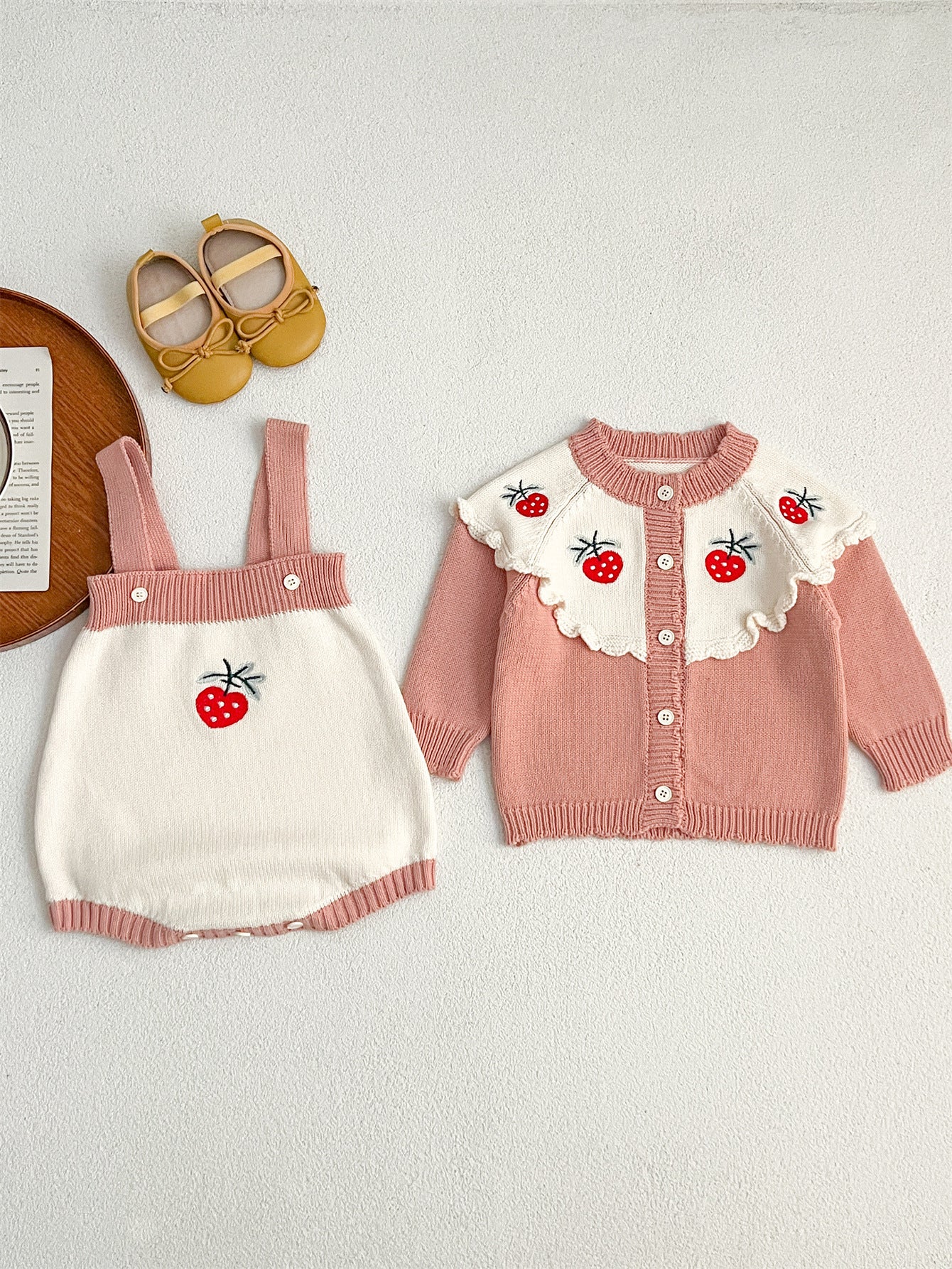 A cute baby girl wearing a long-sleeved knitted top with strawberry embroidery in red and pink colors, perfect for autumn.