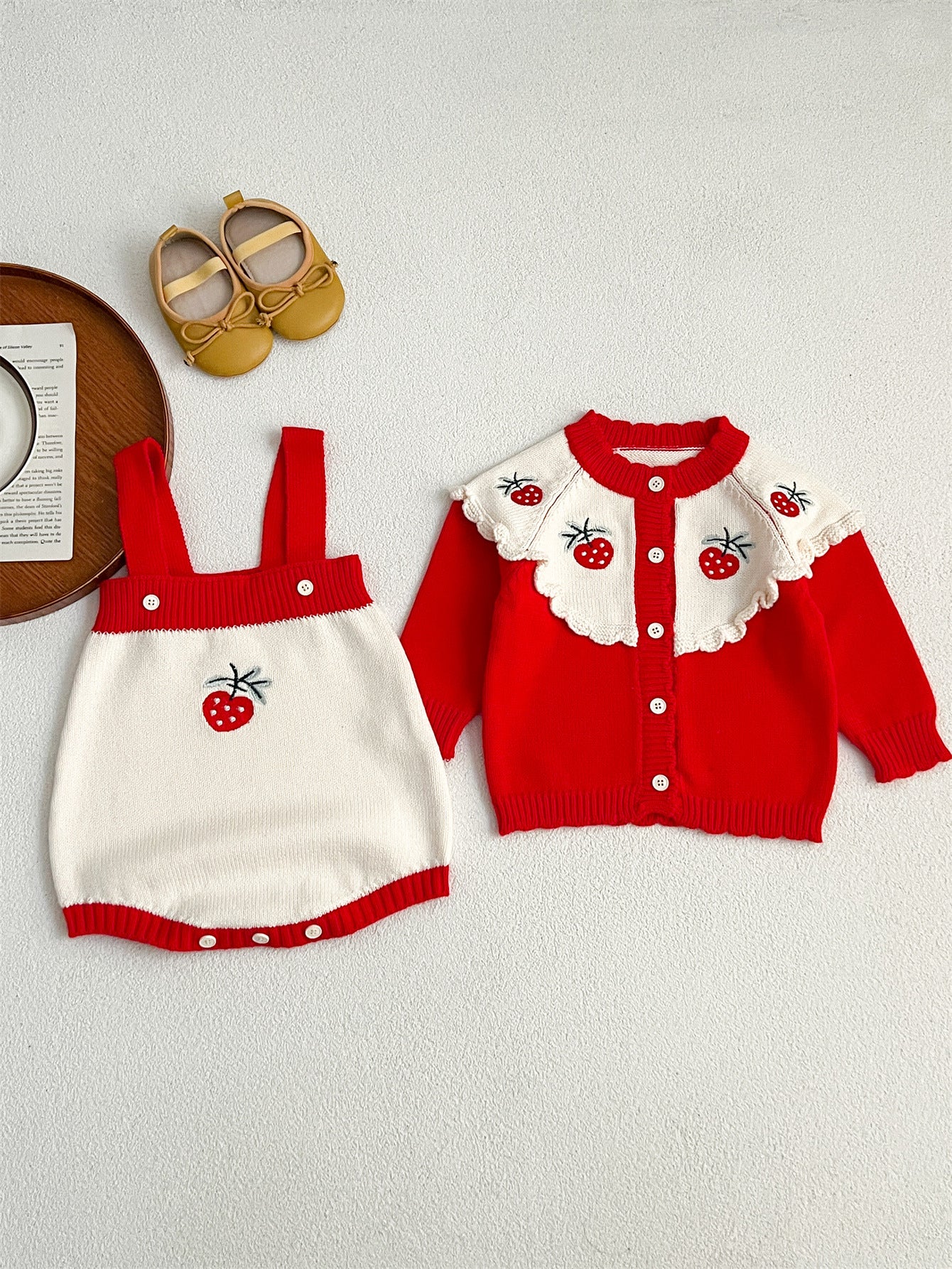 A cute baby girl wearing a long-sleeved knitted top with strawberry embroidery in red and pink colors, perfect for autumn.