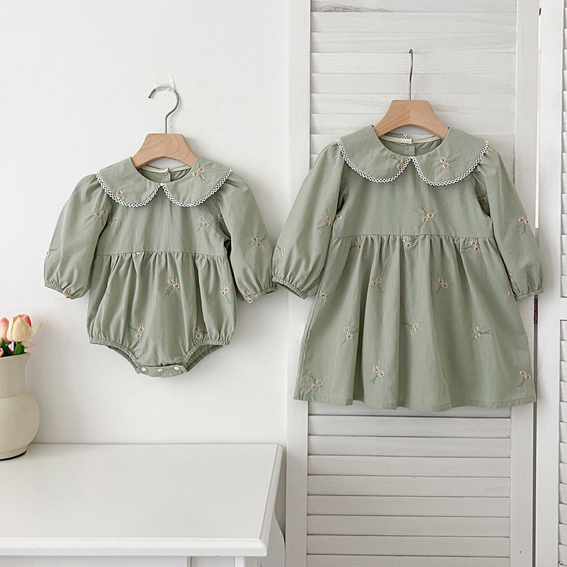 A cute baby girl wearing a long-sleeved green top with daisy floral embroidery, perfect for autumn and spring.