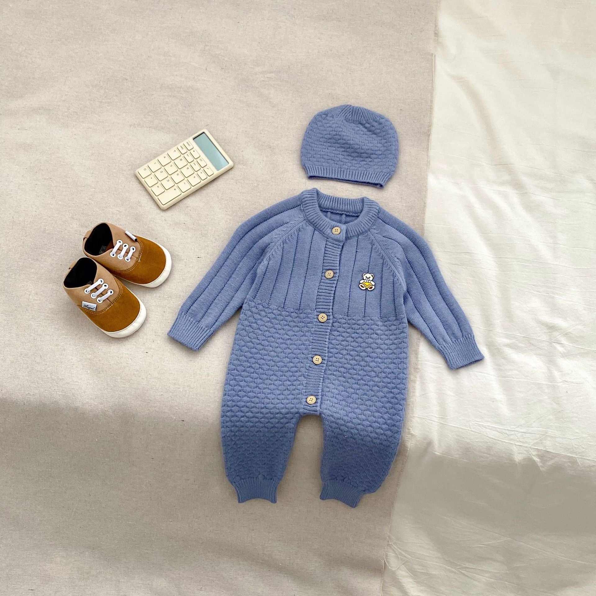 A cozy knitted romper for babies featuring a teddy pattern, available in blue, apricot, and coffee colors, perfect for autumn and winter.