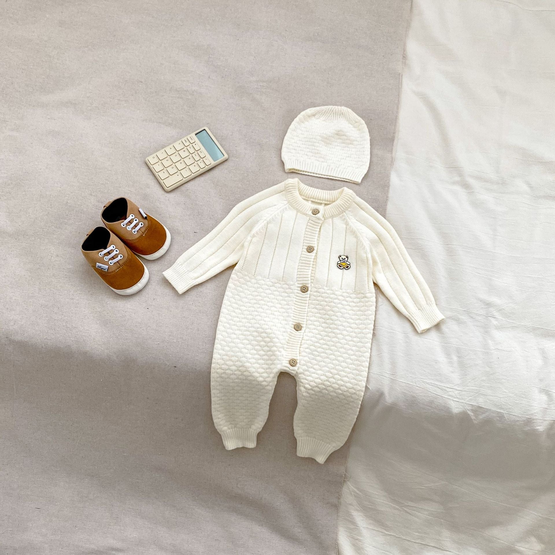 A cozy knitted romper for babies featuring a teddy pattern, available in blue, apricot, and coffee colors, perfect for autumn and winter.