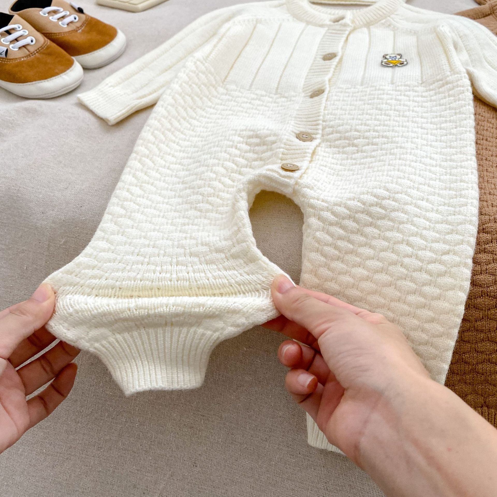 A cozy knitted romper for babies featuring a teddy pattern, available in blue, apricot, and coffee colors, perfect for autumn and winter.