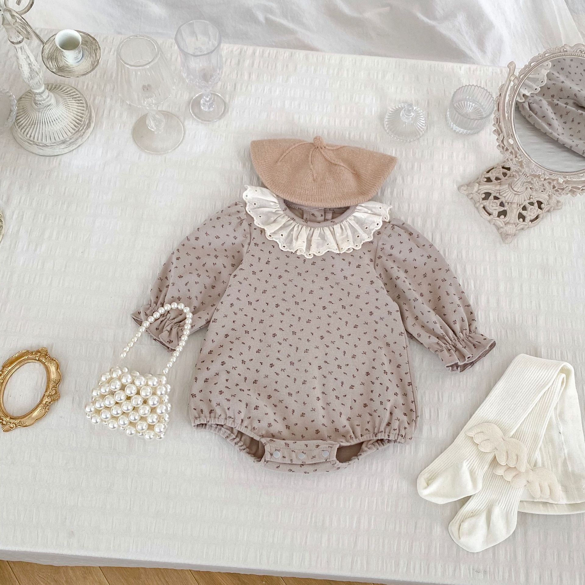 A baby girl wearing a floral print ruffle collar onesie in grey, showcasing long sleeves and a charming design.